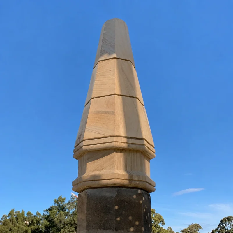 Hand-carved sandstone spire finial standing against a clear blue sky